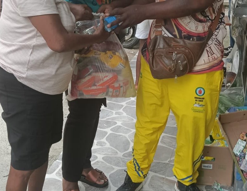 Dos personas se pasan de mano en mano una bolsa de mercado en la calle; los rostros quedan fuera del encuadre.
