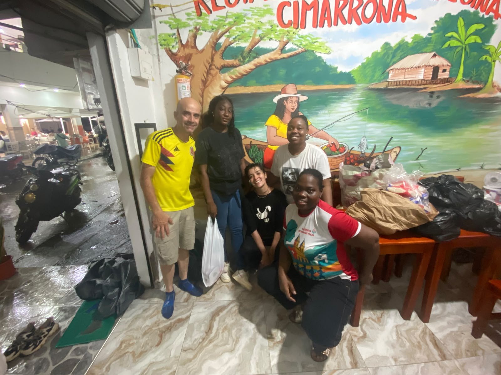Cinco integrantes del equipo posan juntos frente a un mural pintado, al lado de una mesa con las bolsas de mercado listas para entregar.