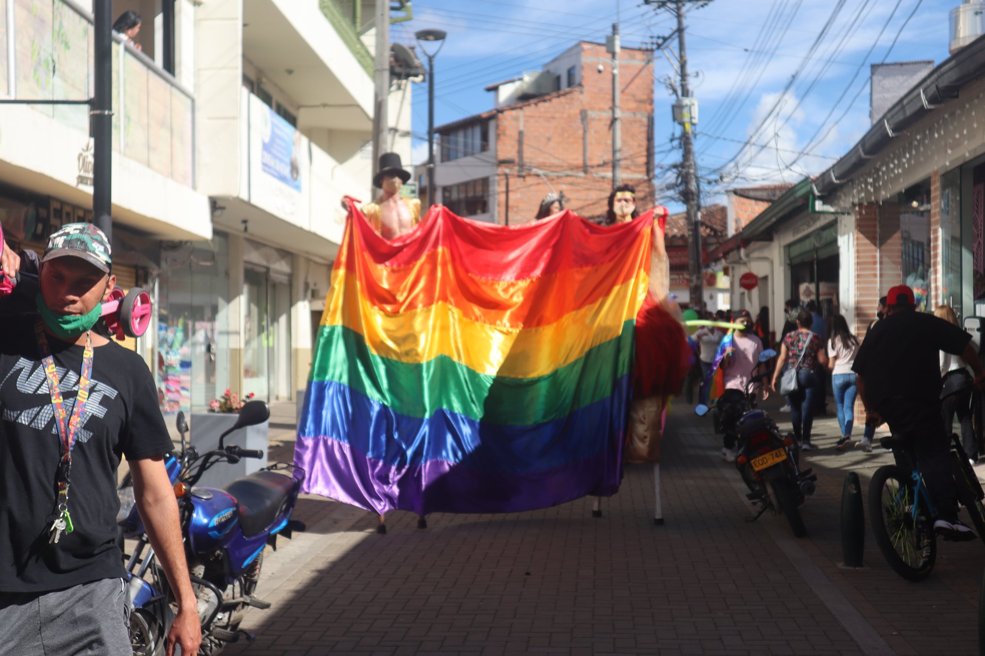 Personas sostienen una bandera multicolor en una calle.