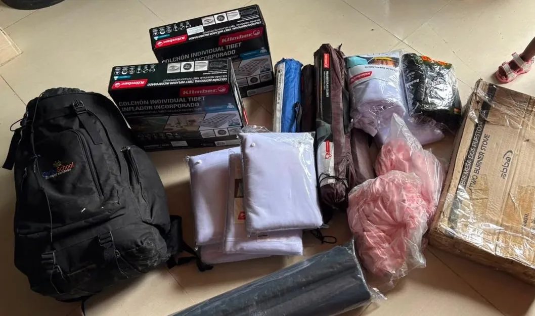 Los artículos comprados extendidos en el piso: cajas de colchones inflables, carpas, toldillos empacados, una estufa de dos puestos y un morral.