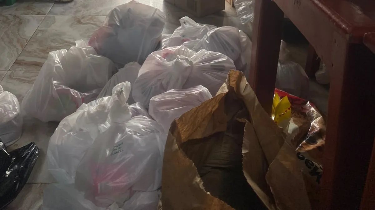 Decenas de bolsas de mercado armadas y apiladas en el piso de un local, listas para repartir.