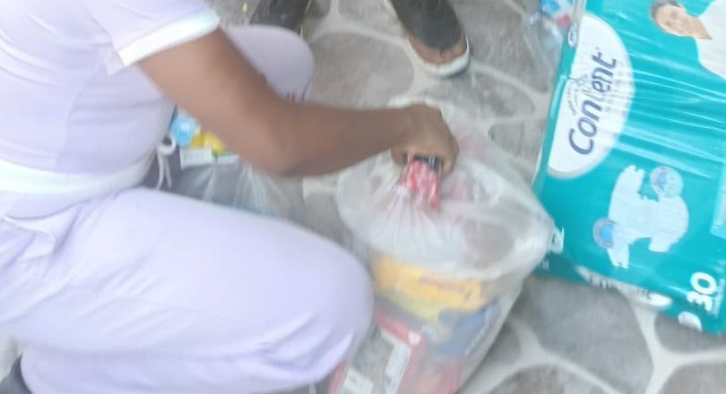 Unas manos cierran una bolsa de mercado en el piso; al lado, un paquete de pañales.
