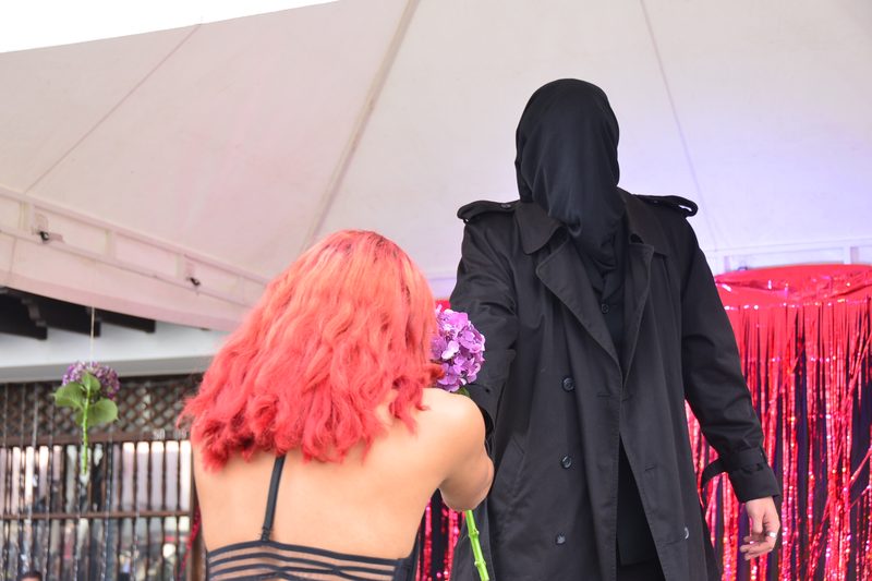 Dos figuras de espaldas están frente a un telón rojo.