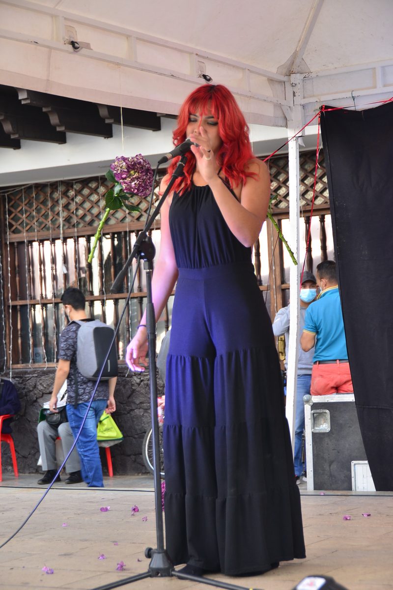 Una artista de cabello rojo habla por micrófono bajo una carpa.