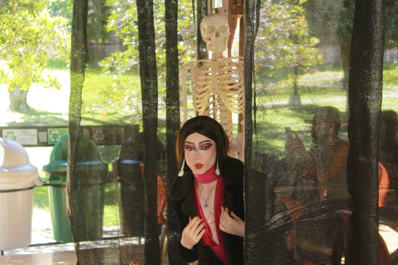 Una artista con maquillaje rojo posa junto a un esqueleto y velos negros.