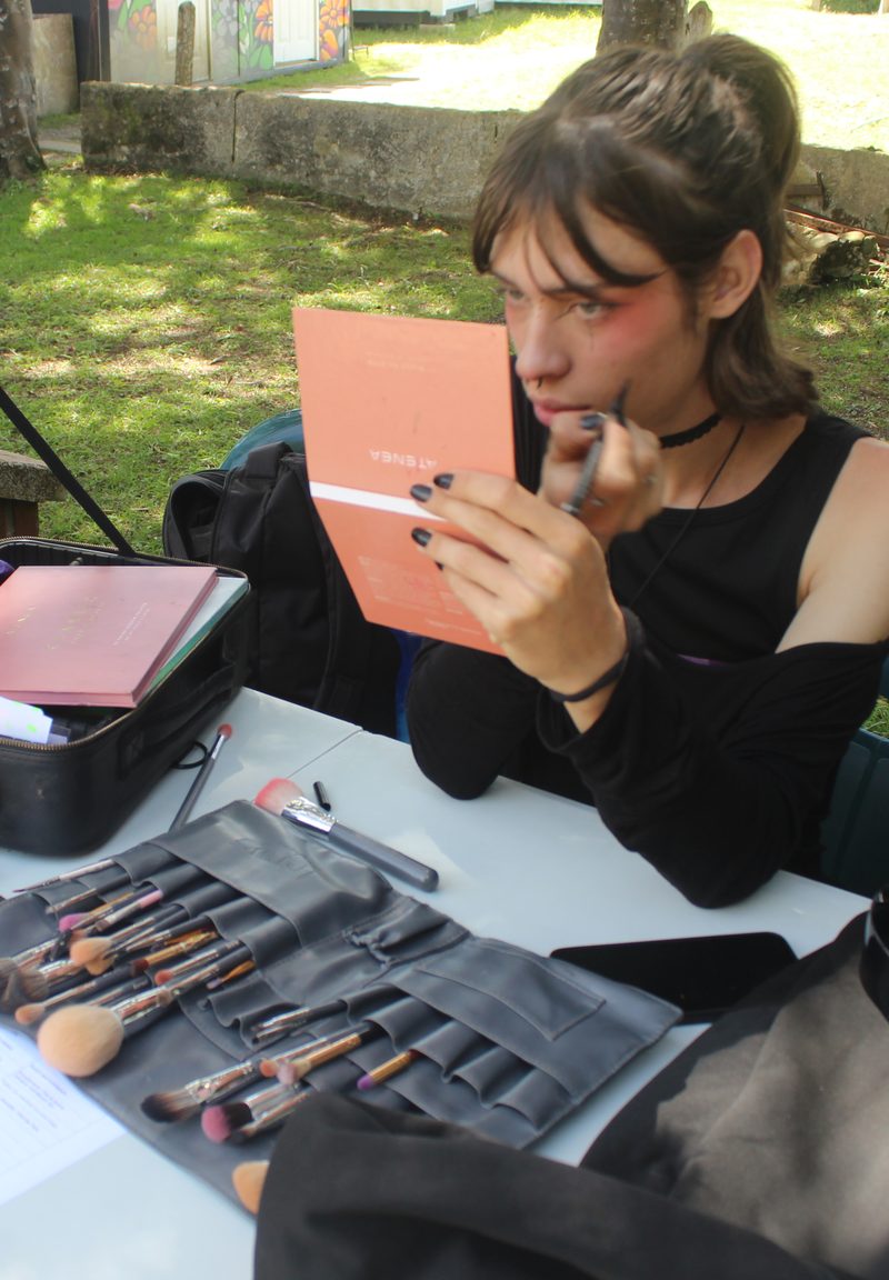 Una persona aplica maquillaje frente a un espejo en una mesa con pinceles.