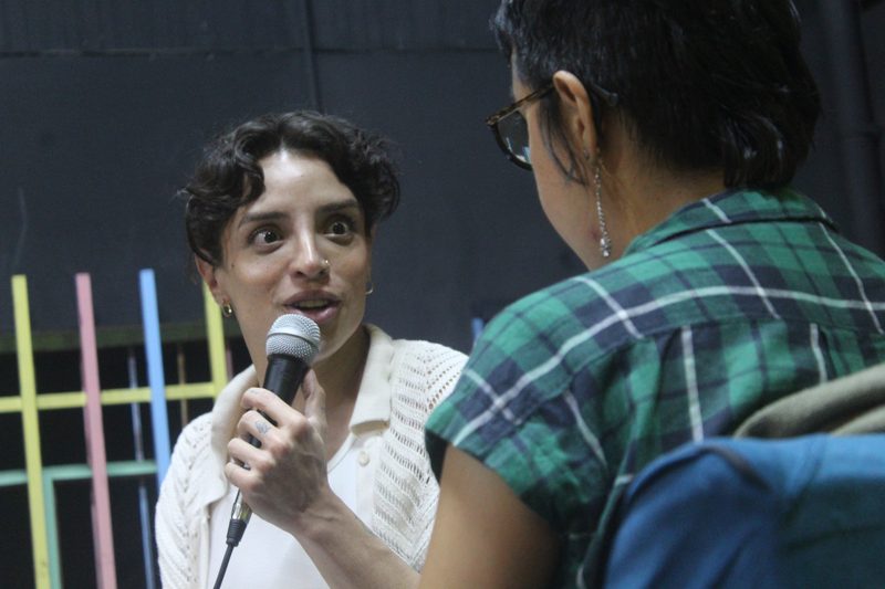 Una persona con micrófono conversa con otra en primer plano.