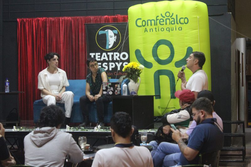 Tres personas adultas conversan frente al público en una sala.