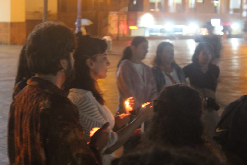 Varias personas adultas sostienen velas encendidas al aire libre.