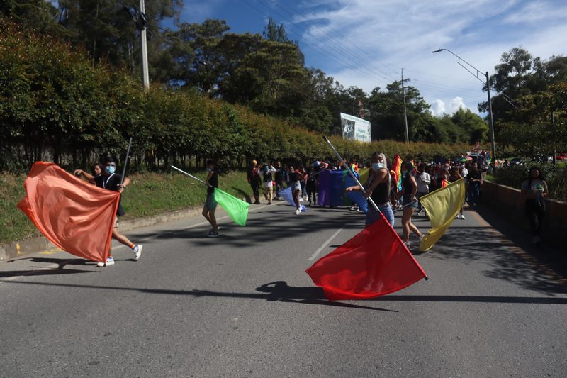 Personas mueven banderas de colores sobre una vía.