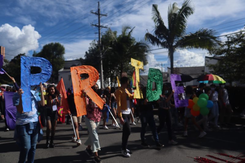 Personas marchan llevando letras grandes que forman la palabra PRIDE.