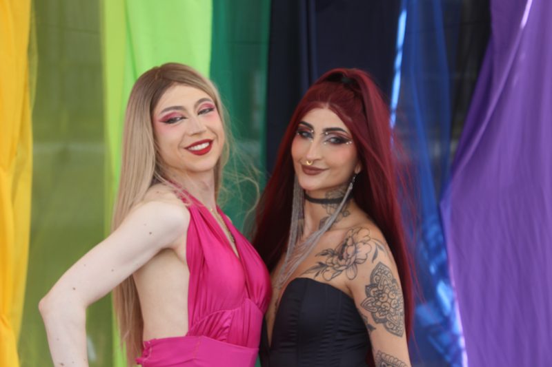 Dos artistas posan juntas frente a cortinas de colores.