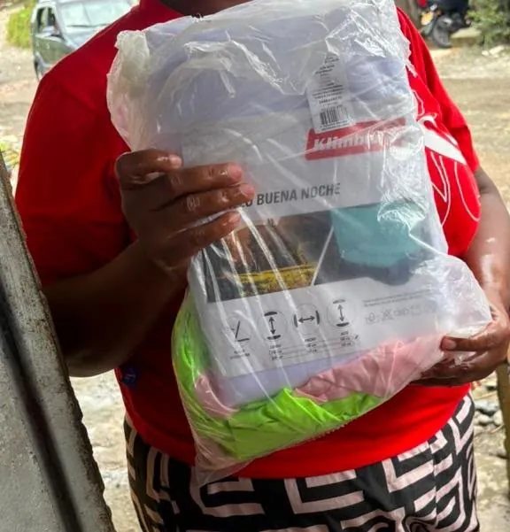 Unas manos sostienen contra el pecho un paquete de ropa de cama todavía empacado.